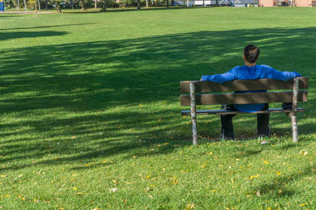 Toronto, Canada, October 2016 - Man in blue outfit sitting with outstretched arms on a bench in a park on a sunny autumn dayのeditorial素材