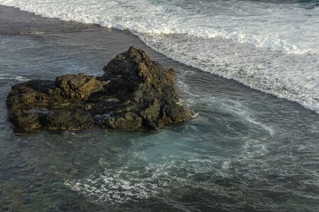 Big rock in the sea with approaching foamy waves