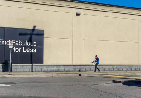 Male adult with face mask carries his shopping bags while walking along the wall of the store