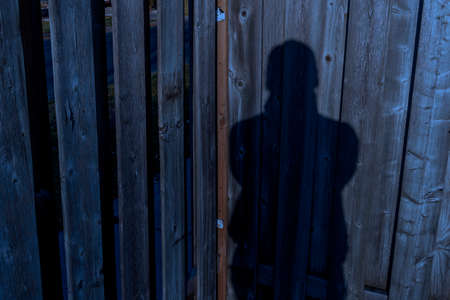 Shadow of human shape on a wooden fence at nightfall
