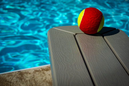 A red and yellow ball on a bench by a pool