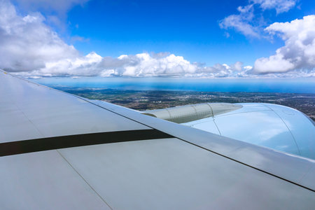 The aircrafts wing is silhouetted against a blue sky with fluffy cumulus clouds, showcasing the beauty of air travel and the wonders of aviationの写真素材