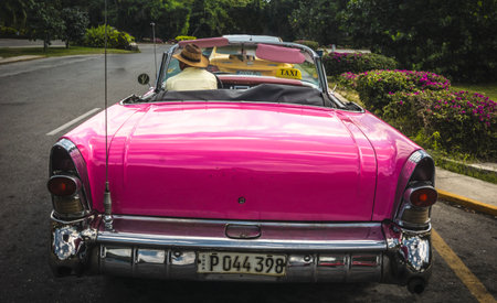 Pink vintage cuban taxi cab with driver parked on a road