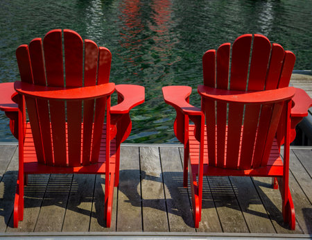 Pair of red outdoor chairs on a wooden deck facing the lakeの写真素材