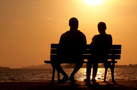Silhoutte of a couple sitting on a bench in contemplation in front of a lake at duskの素材