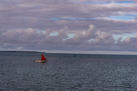 One boat with red sail on a calm open seaの写真素材