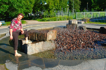 Beautiful middle-aged woman in a city park near the fountainの写真素材
