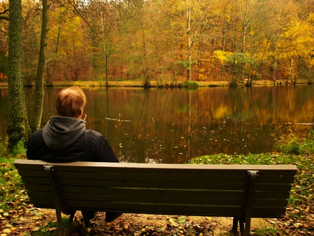 A middle aged man resting on a bench by the lakeの写真素材