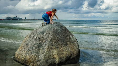 A girl in red with long hair climbed on a big stone on the seashore