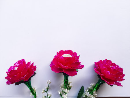 Handcrafted artificial flower with vibrant pink petals and green leaves on a white background. A decorative craft symbolizing beauty and creativityの写真素材
