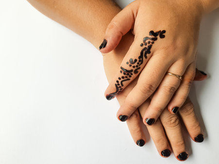 Close up of hands with a black henna tattoo design and black painted nails on a white background.の写真素材