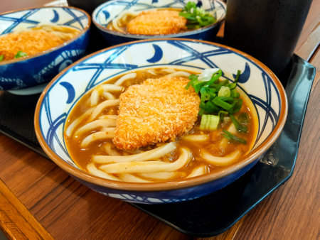 Close-up of chicken katsu curry udon served in a Japanese restaurant. Thick udon noodles in savory curry broth topped with crispy fried chicken and chopped scallionsの写真素材