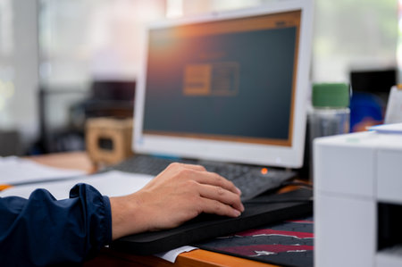 Male office worker's hand holding a mouse to use a desktop computer.の写真素材