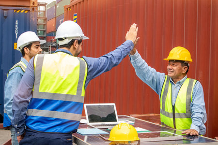 Happy male technicians team in safety helmets and uniforms giving each other high-fives and smiling while working together at the workplace, happiness at work conceptの写真素材