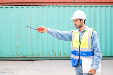 A male worker in a container shipping company using a laptop and reported through a walkie-talkieの写真素材