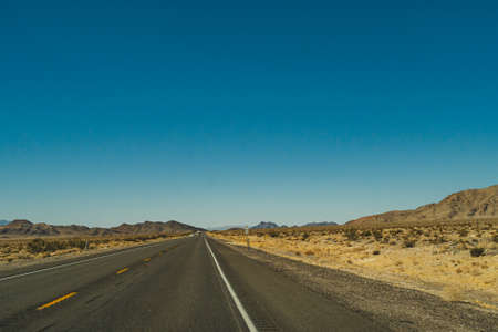 Two lane road in the arid Sierra Nevadas leading to mountains against blue skyの写真素材