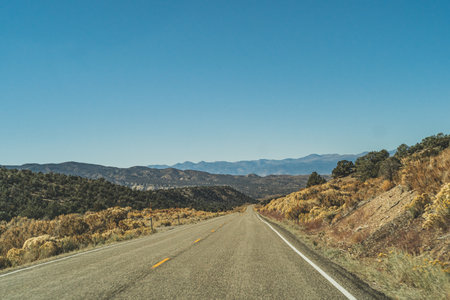 Two lane road in the arid Sierra Nevadas leading to mountains against blue skyの写真素材