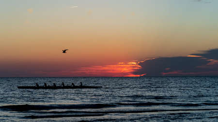 Rowing crew in silhouette on water against pastel sunset skyの写真素材