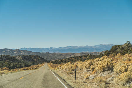 Two lane road in the arid Sierra Nevadas leading to mountains against blue skyの写真素材