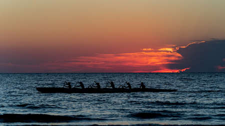 Rowing crew in silhouette on water against pastel sunset sky
