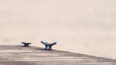 Rusting mooring cleat on old dock against out of focus water backgroundの写真素材