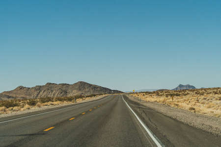 Desert highway road leading to the horizon against clear blue sky and mountainsの写真素材