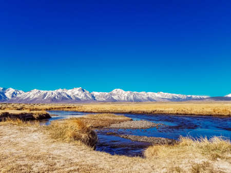 River runs though Arid plain against Sierra Nevada Mountains blue skyの写真素材