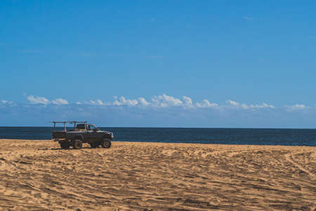 Off road vehicle on sandy beach against blue sky and oceanの写真素材