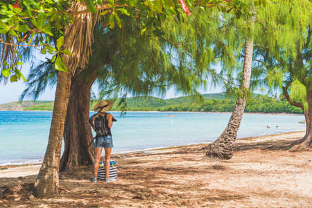 Woman with straw hat and striped bag on tropical beach near treeの写真素材