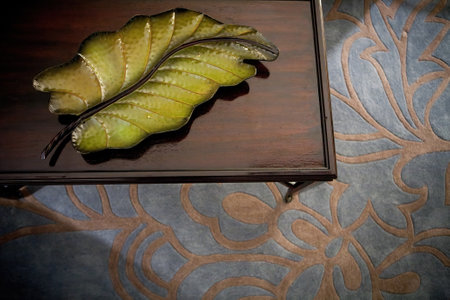 Top view of coffee table with glass decoration in shape of green leaf on a gray carpet with patternの写真素材