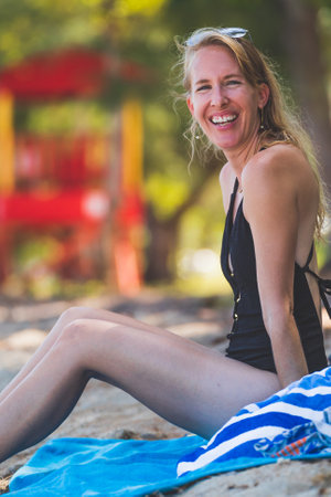 Happy woman smiling at camera on tropical beach sitting in swimsuit towelの写真素材