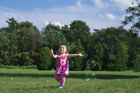 Little Girl Wearing Pink Outfit, Catching Bubbles in Grassy Parkの写真素材