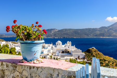 Ceramic pot with blooming geraniums on the parapet against the sea and the town is a typical Cycladic view, Plaka, Milos, Cyclades, Greece.の写真素材