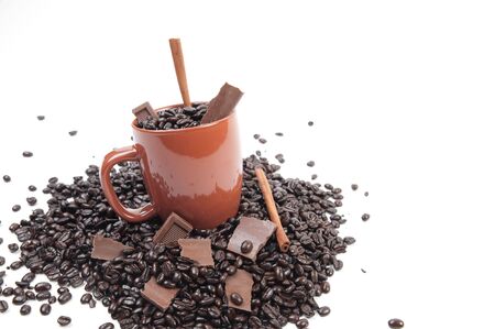 Coffee mug full of coffee beans on pile of coffee beans with chocolate and cinnamon sticksの写真素材