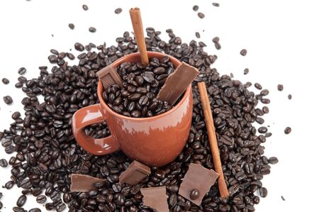 Coffee mug full of coffee beans on pile of coffee beans with chocolate and cinnamon sticksの写真素材