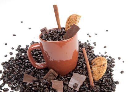 Coffee mug full of coffee beans on pile of coffee beans with chocolate and cinnamon sticksの写真素材