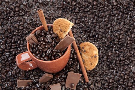 Coffee mug full of coffee beans on pile of coffee beans with chocolate and cinnamon sticksの写真素材