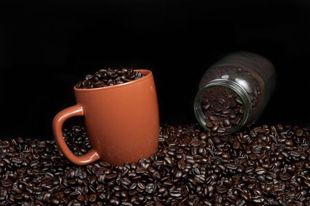 coffee mug full of coffee beans on pile of coffee beans with a jar of ground coffeeの写真素材