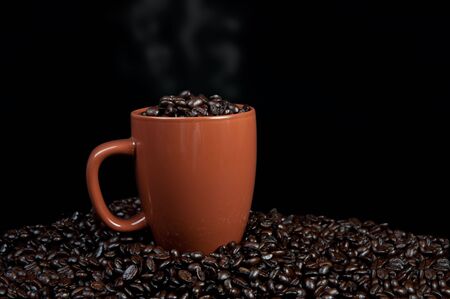 Cup of coffee beans with cup on top of coffee beans with steam coming out of cupの写真素材