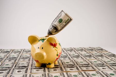 $100 bills in US currency with piggy bank on top of moneyの写真素材