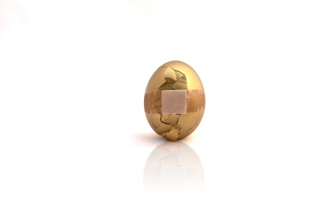 Broken golden egg with bandage over cracked area on white backgroundの写真素材