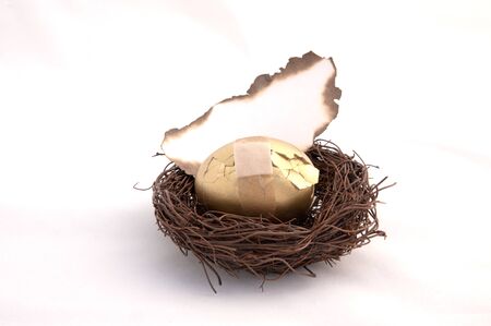 A golden egg sitting in a birds nest with a  blank piece of paper burning. Representing your savings going up in smokeの写真素材