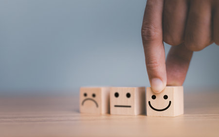 Close up customer hand choose smile face and blurred sad face icon on wood cube, Service rating, Customer service evaluation and satisfaction survey concepts.の写真素材