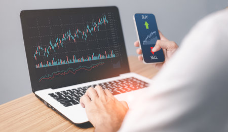 Male trader investor analyst holding smartphone in hand analyzing stock market trading charts...