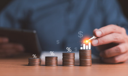 Businessman using a stylus to interact with a digital growth graph on stacked coins, representing financial investment, increasing profit, and future success in the digital economy.の写真素材