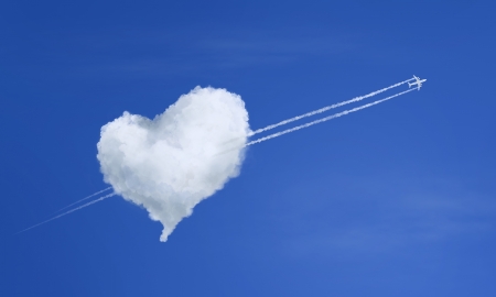 Airplane flying through heart shaped cloudの写真素材