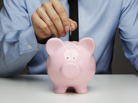 Male hand putting coin into a piggy bankの写真素材