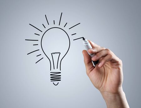 Male hand drawing light bulb over dark backgroundの写真素材