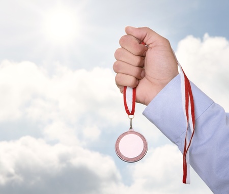 Businessman holding blank gold medal over cloudy sky with copy spaceの写真素材