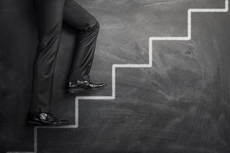 Businessman climbing at the career stairs drawn on a black chalkboard with copy spaceの写真素材